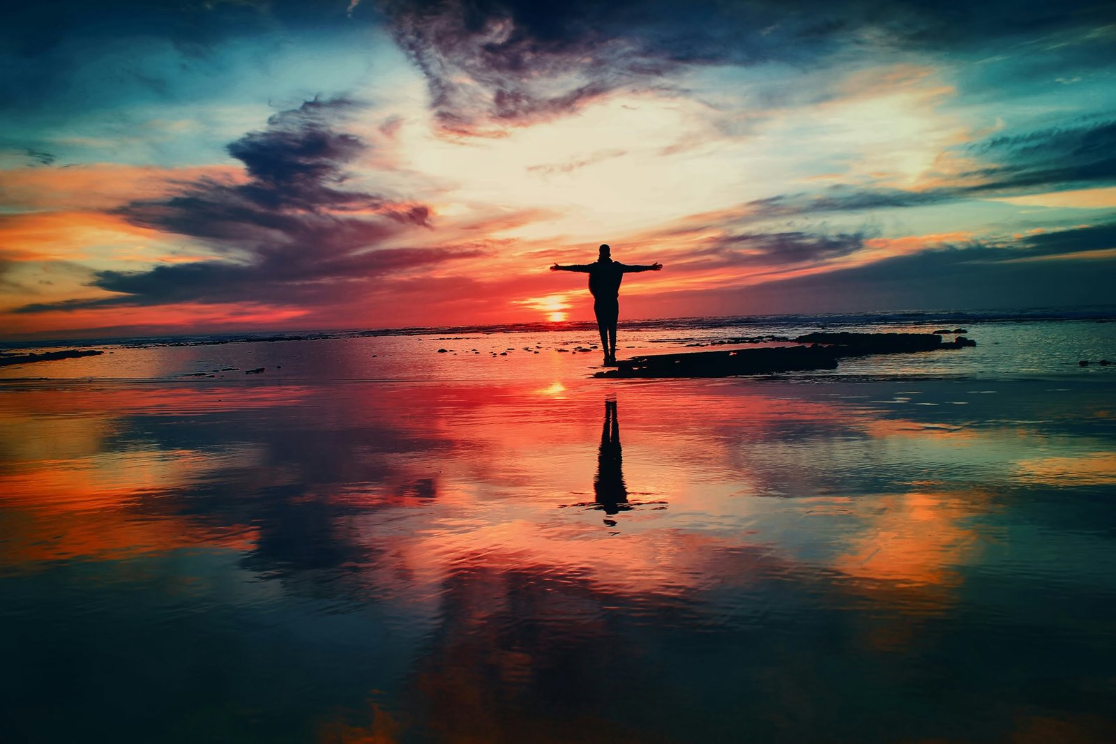 silhouette of person standing on rock surrounded by body of water